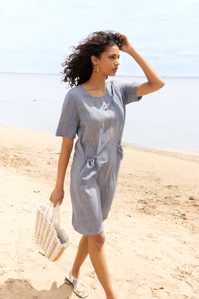 Images show the Alison Sheri Relaxed Pocket Dress A47072 in Sand and Indigo from the front and side, highlighting the round neckline, relaxed fit, elbow-length sleeves, side pockets with gentle cinching effect, and the fluid drape of the lightweight linen-blend fabric.