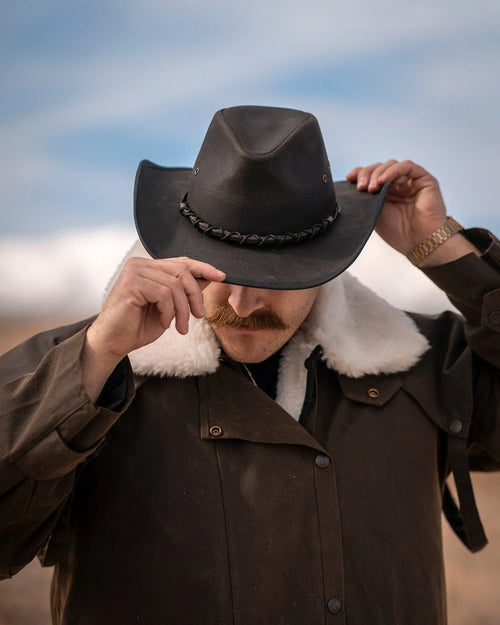 Bootlegger Oilskin Hat in black by Outback Trading Co., showcasing its structured crown, wire brim, chin cord, and moisture-wicking sweatband. Photos include front, side, and rear views highlighting the hat’s rugged material, shape, and functional details.